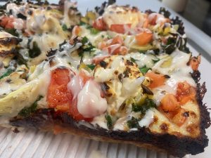 Closeup photo of pizza with melted cheese, tomatoes, and artichokes.